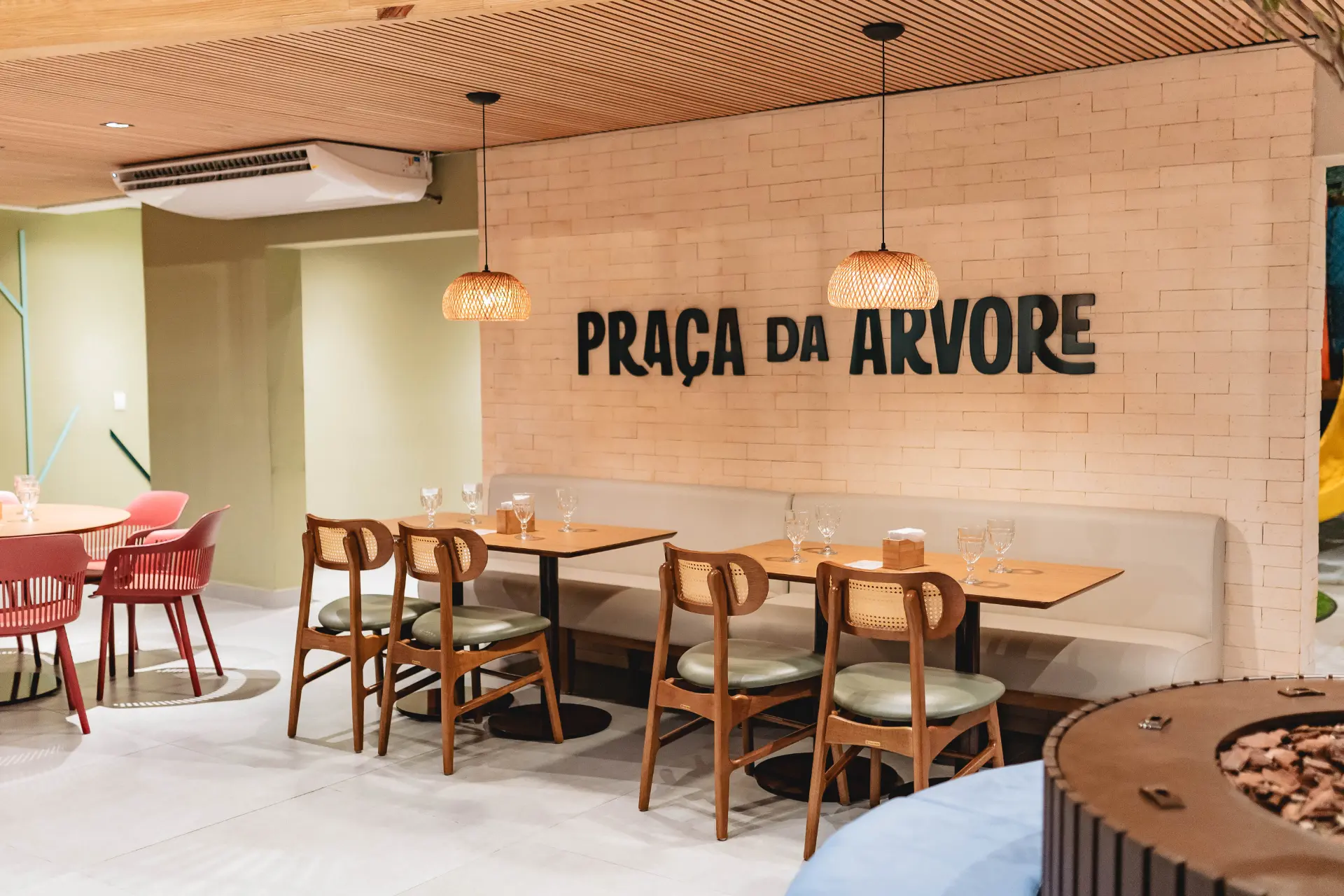 Área de convivência da Praça da Árvore com mesas e parede da marca